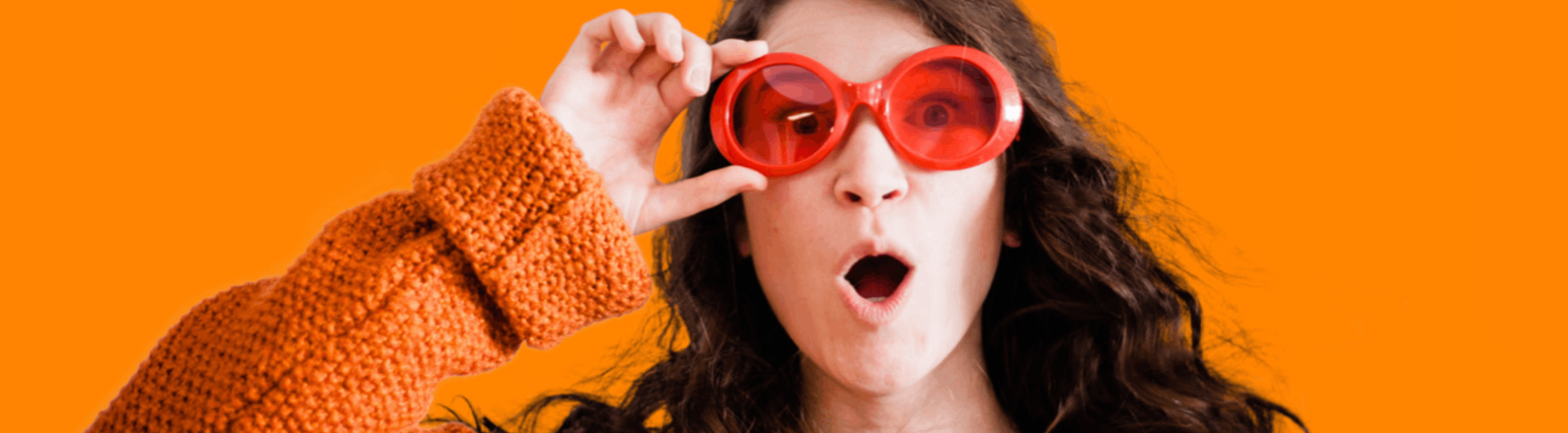 Une femme avec un air surprise tient de la main droite des grosses lunettes rouges