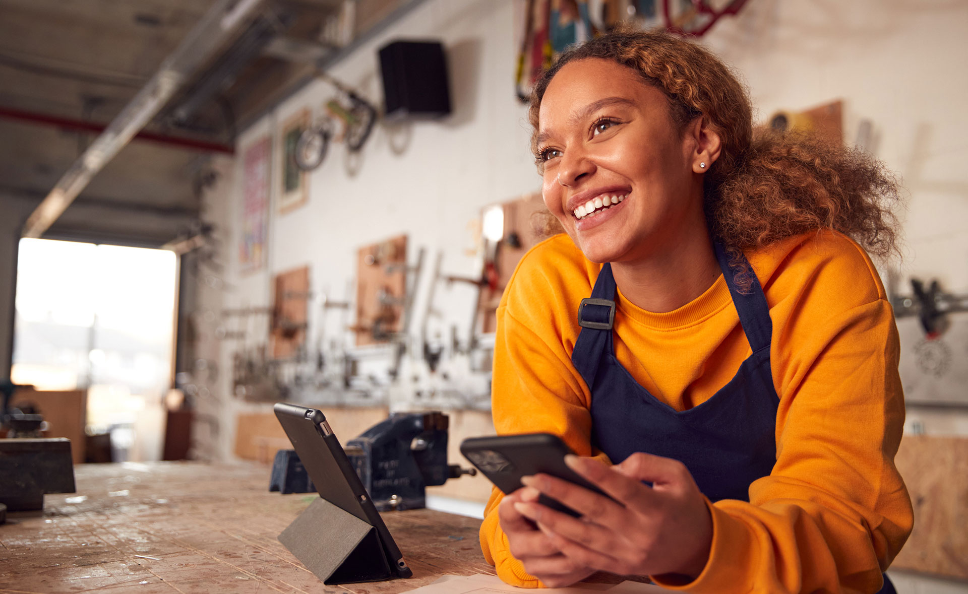 Jeune femme souriante accoudée à un comptoir, tenant un téléphone intelligent dans ses mains