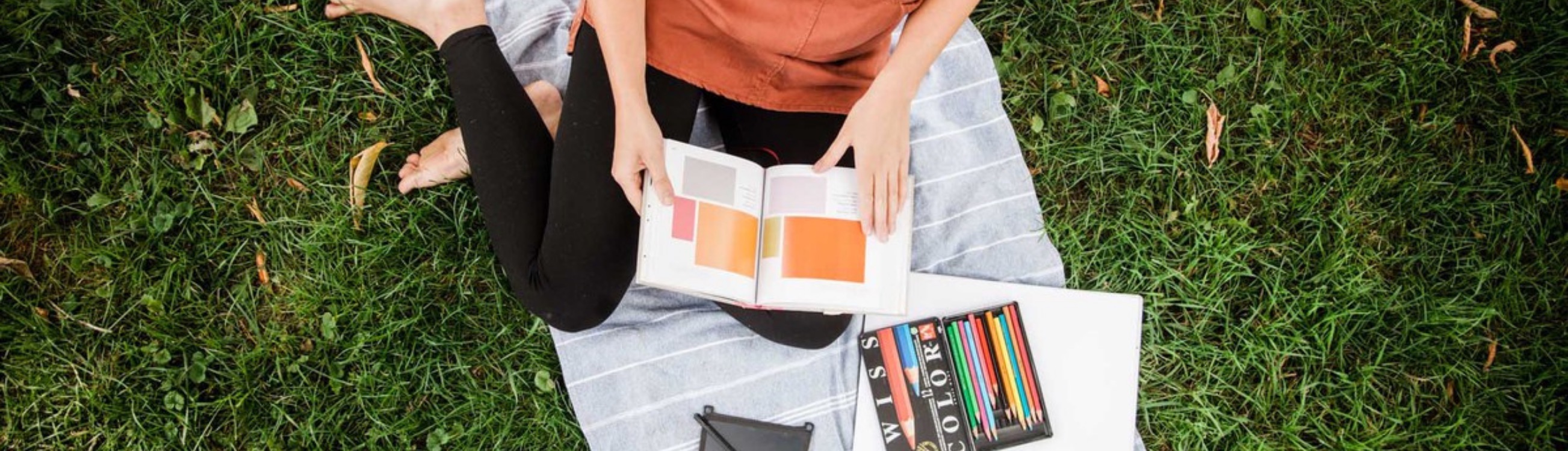 Une personne est assise sur un tapis dans l'herbe en lisant un livre sur les couleurs 