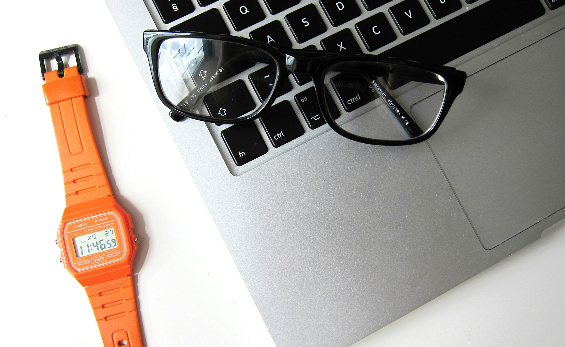 Lunettes sur un ordinateur ouvert et montre orange à la gauche de l'ordinateur